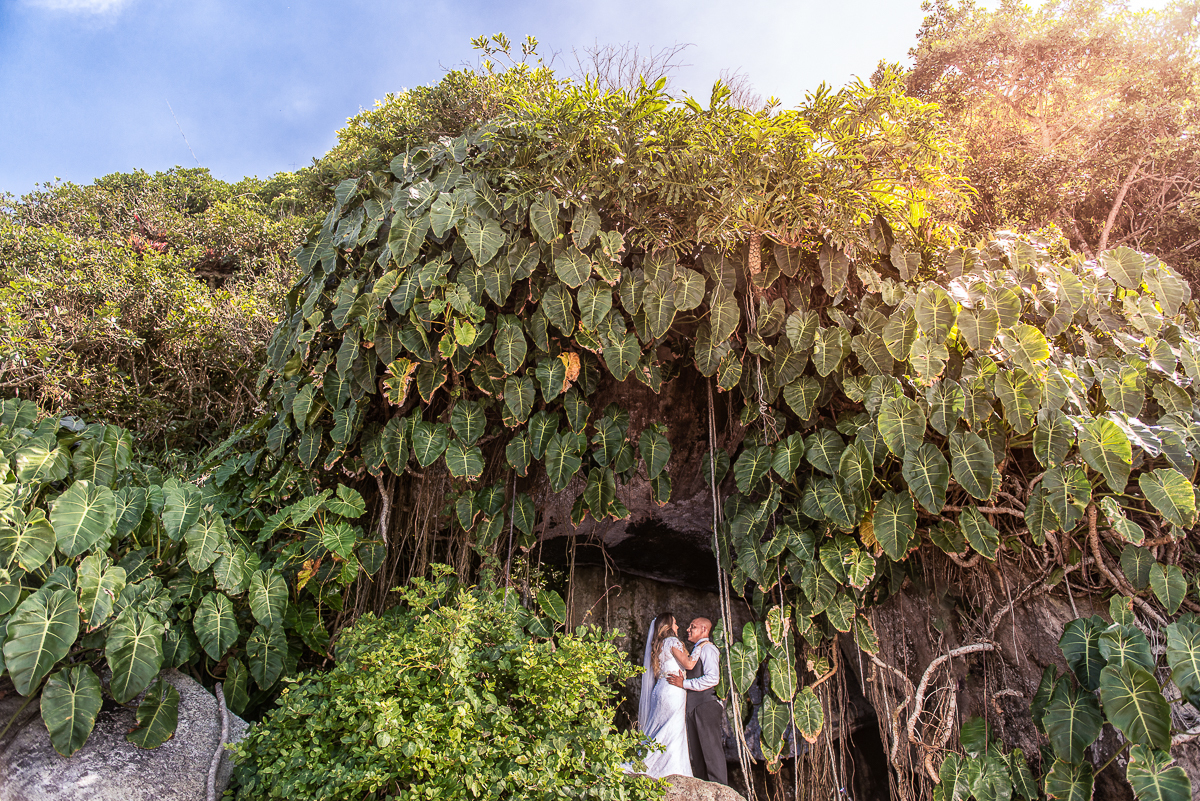 Fotografia na entrada da caverna formada por pedras e um belo verde com céu azul, casal amou o trash the dress deles.