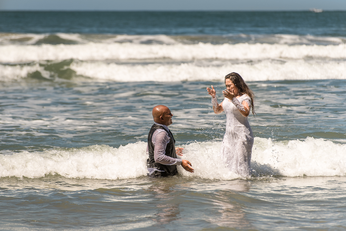 casal brincando de jogar água um no outro na água do mar.