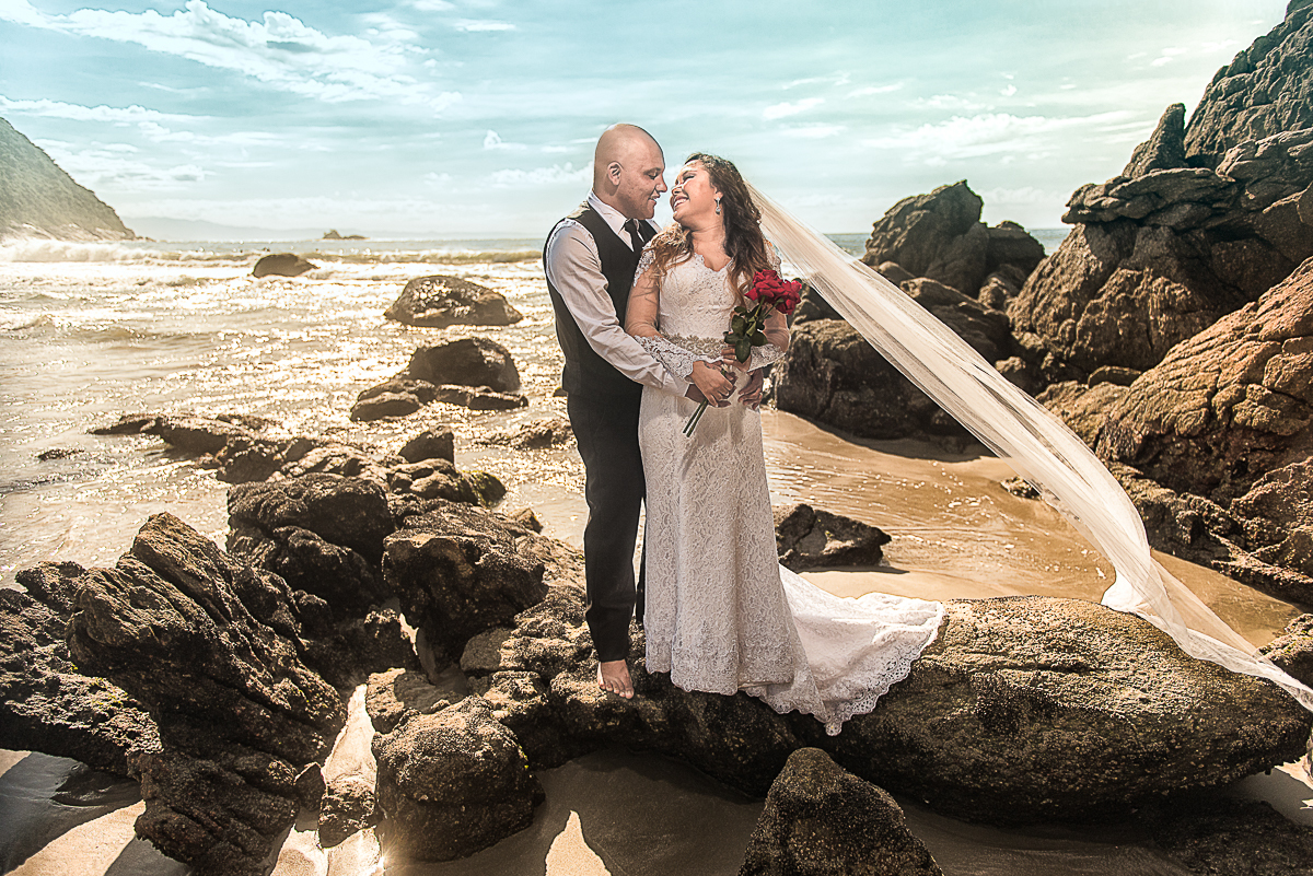 Noivos em imagem espetacular sobre as pedras da praia do Guarujá.