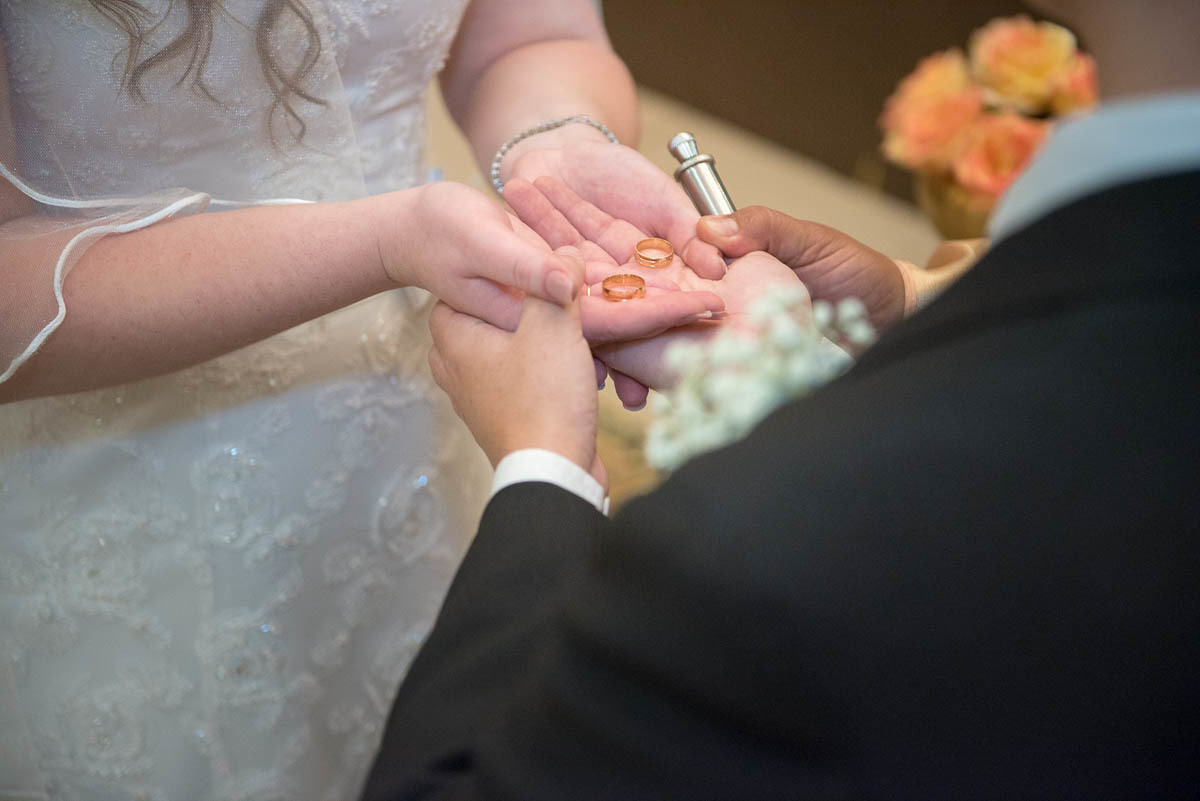 Noiva segurando as alianças de seu casamento junto com o noivo.