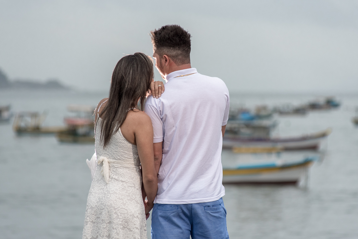 Casal admira vista com barcos de pesca ao redor na praia de Perequê, ensaio de casal.