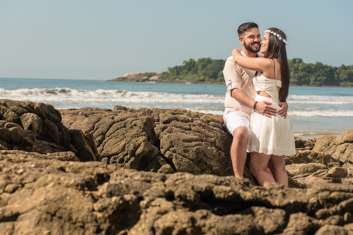 Nas pedras da praia de Iporanga no Guarujá, casal com mar ao fundo em bela foto do ensaio pre wedding.