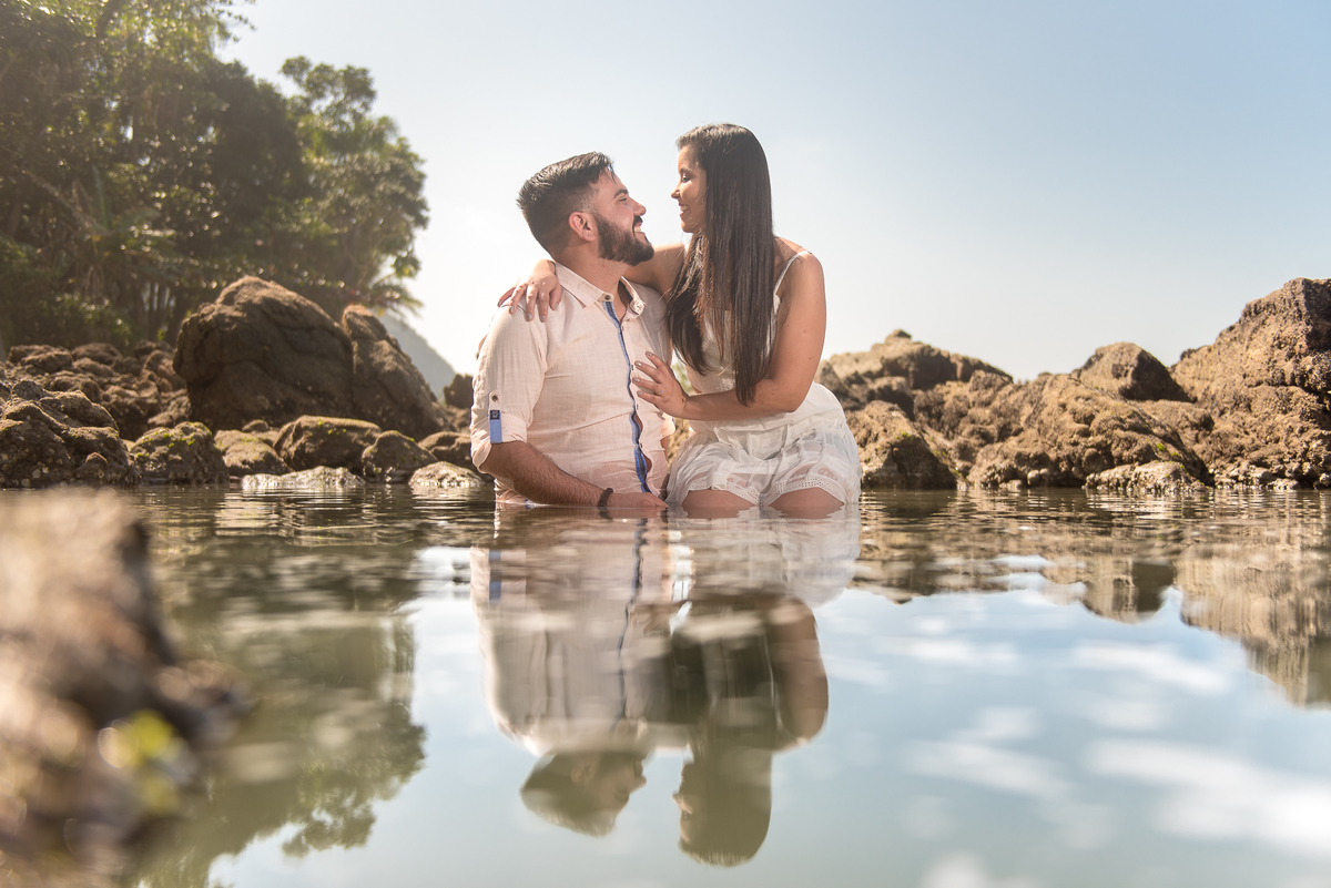 Dentro de uma piscina natural o casal se beija e se olha apaixonados