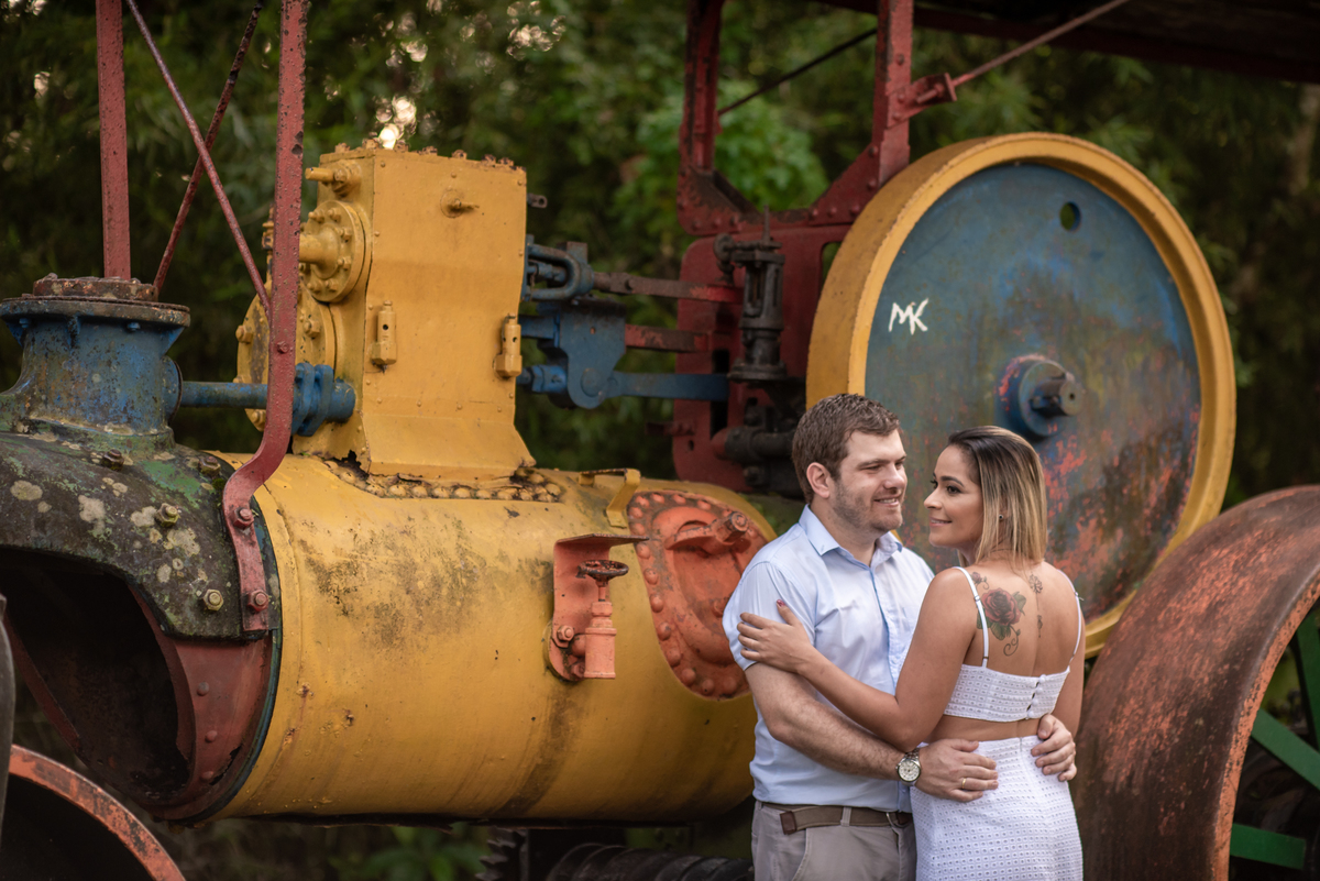 Casal abraçado em frente maquina de pavimentação antiga no parque cemucam em ensaio pré wedding.