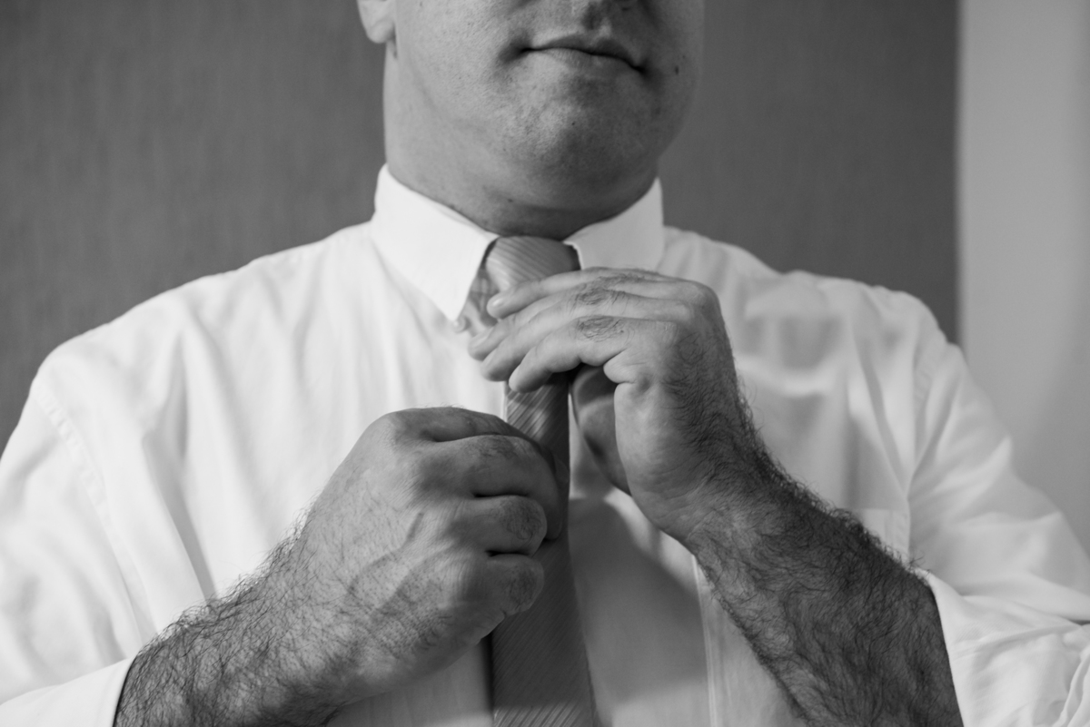 Noivo dando um nó na gravata se preparando para o casamento.