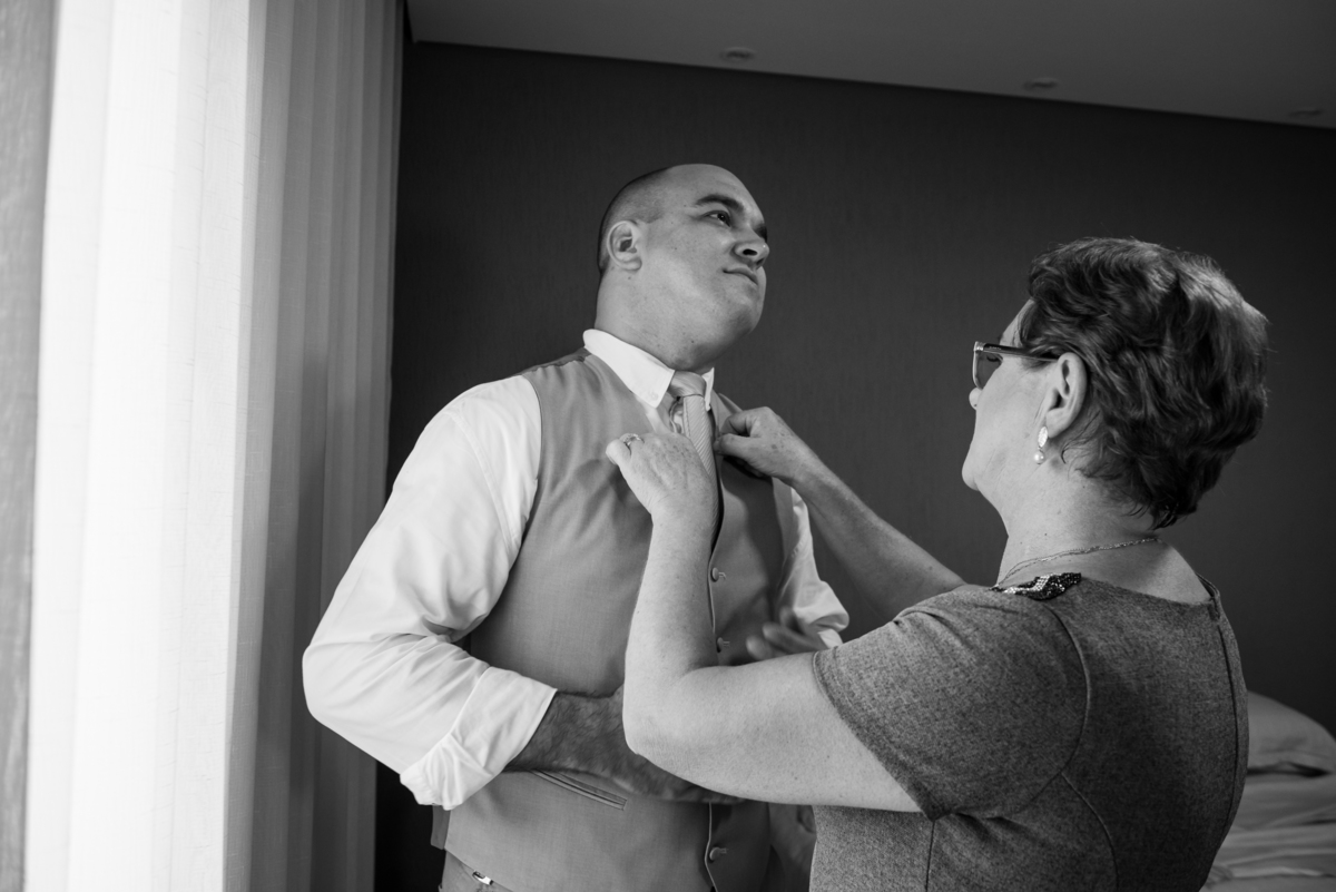 Mãe do noivo ajudando o filho a se arrumar antes do casamento.