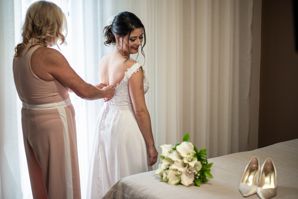 Mãe da noiva ajuda noiva a colocar o vestido de seu casamento.