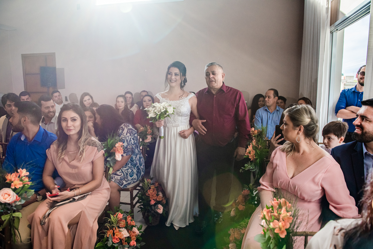 Noiva entra com seu pai para se casar na sala de sua casa.