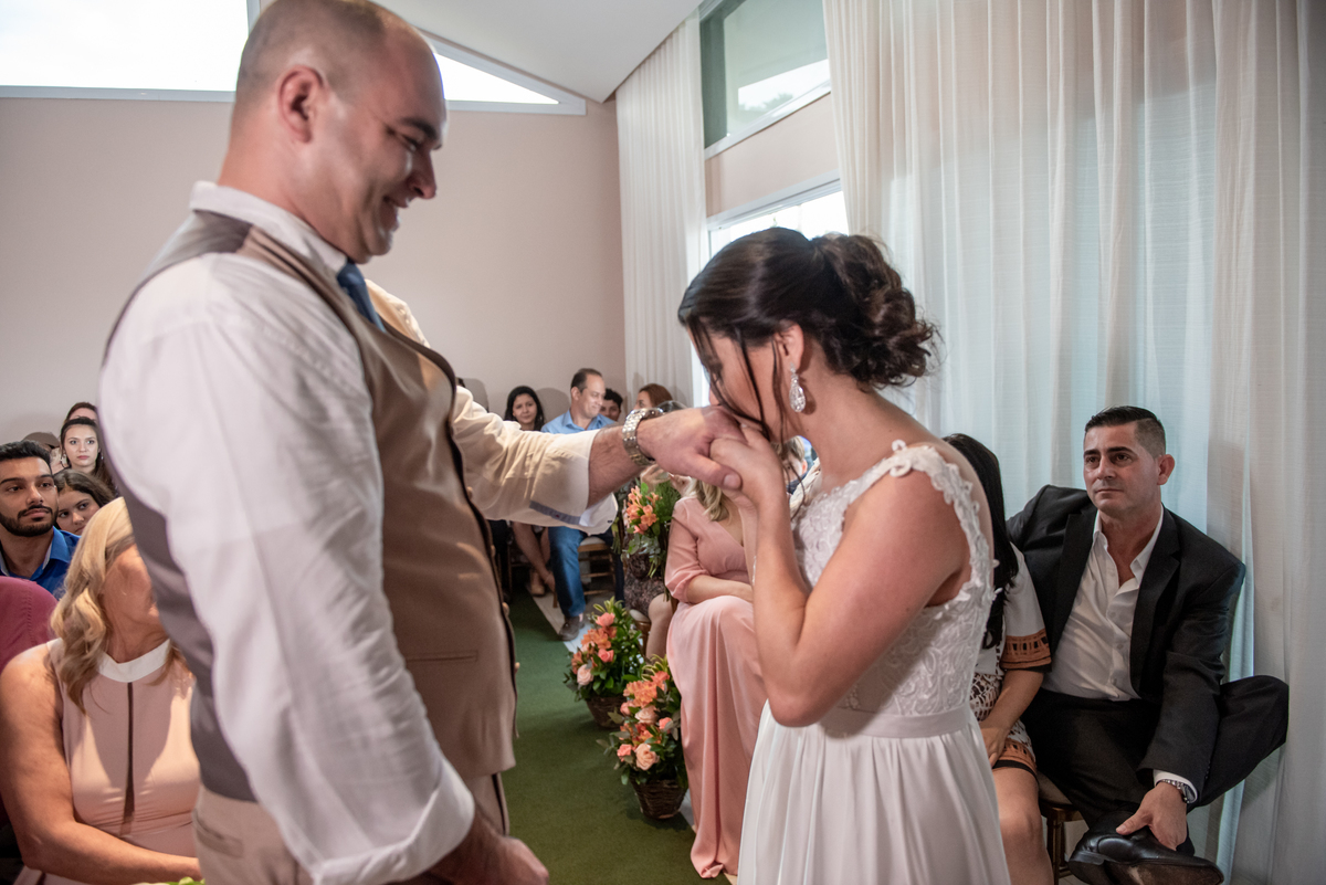 Noiva beija a mão do noivo em cerimonia de casamento civil.