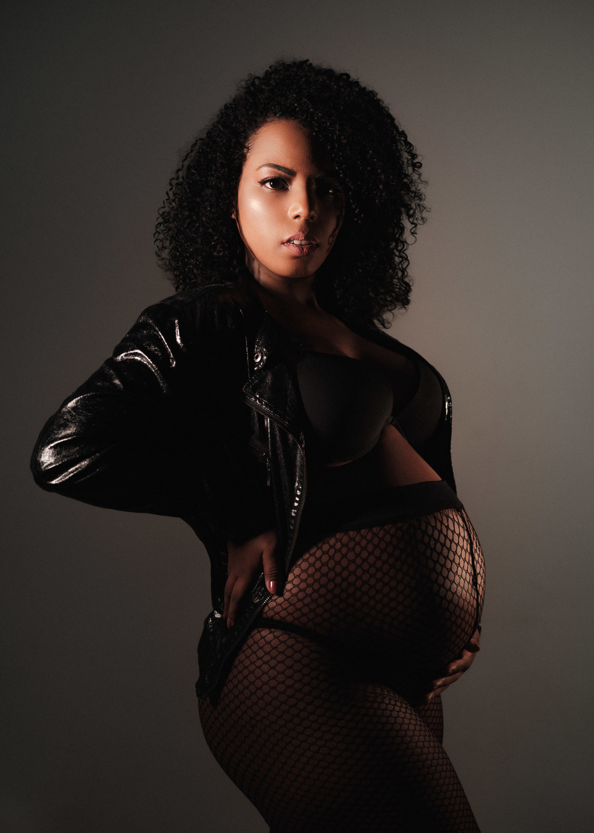 foto de gestante em estudio com meia arrastão e jaqueta de couro preta