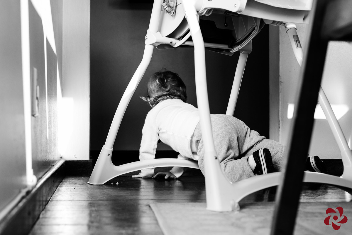 Otávio brinca de gatinhar embaixo da mesa entre as cadeiras.