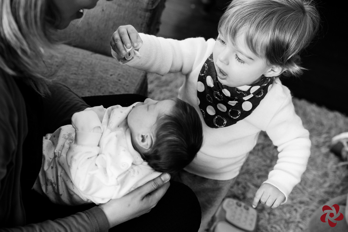 O irmão mais velho, Otávio, brinca de tirar a chupeta da irmã recém nascida, que está no colo da mãe.