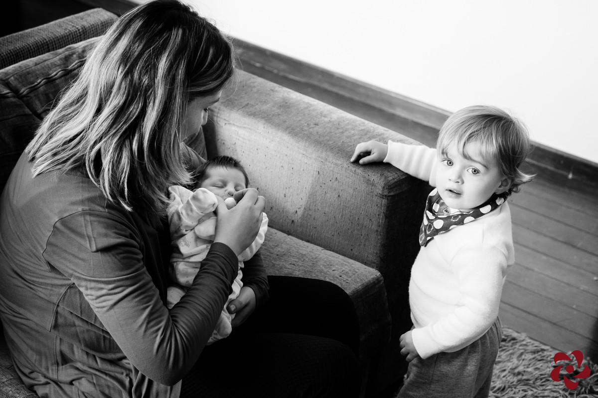 Natácia está sentada no sofá da sala com a Júlia no colo e Otávio, o filho mais velho, está ao lado olhando para a câmera.