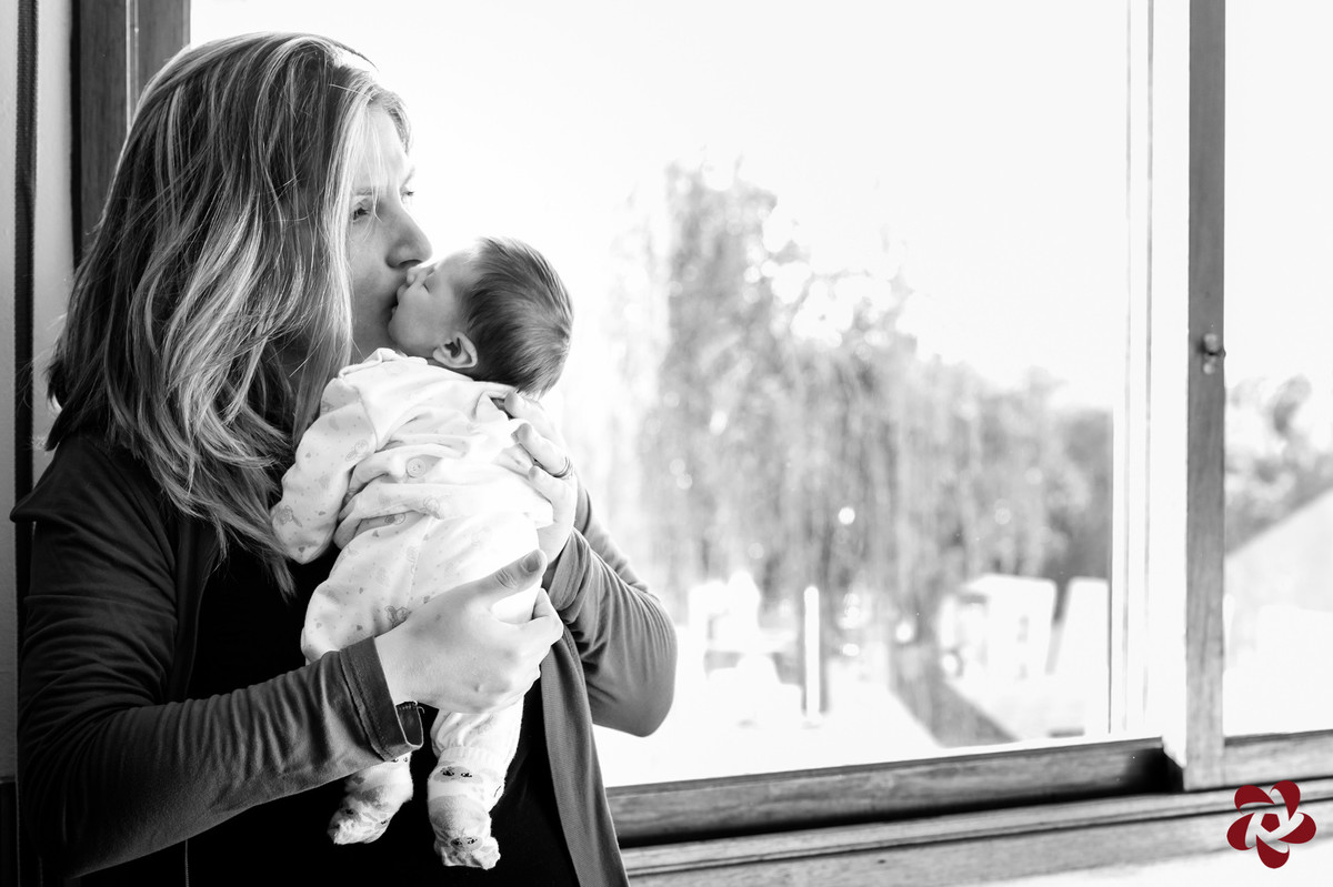 A mãe está com a filha mais nova no colo, iluminada pela luz da janela.