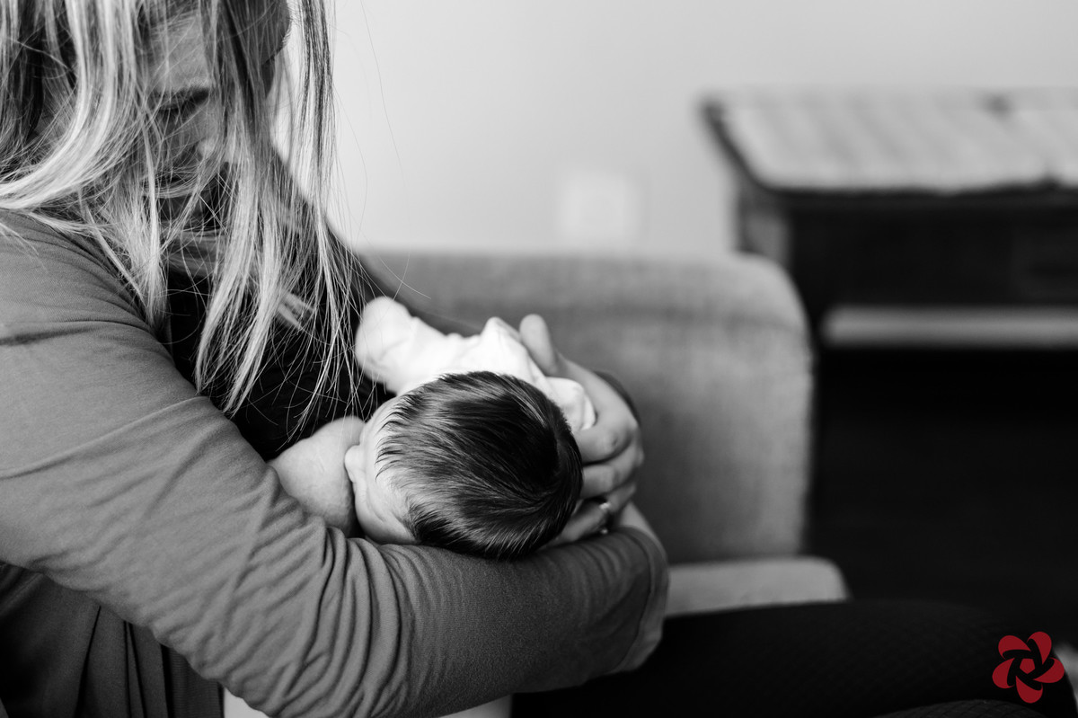 Natácia está sentada no sofá amamentado a filha. O close da foto está no carinho da mãe no cabelo da filha.