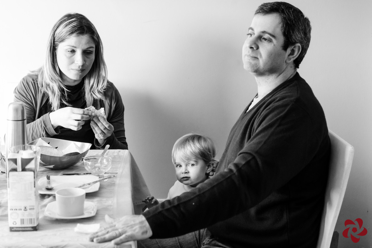 O casal está sentando na mesa de café da manhã e Otávio olha atentamente para a câmera.