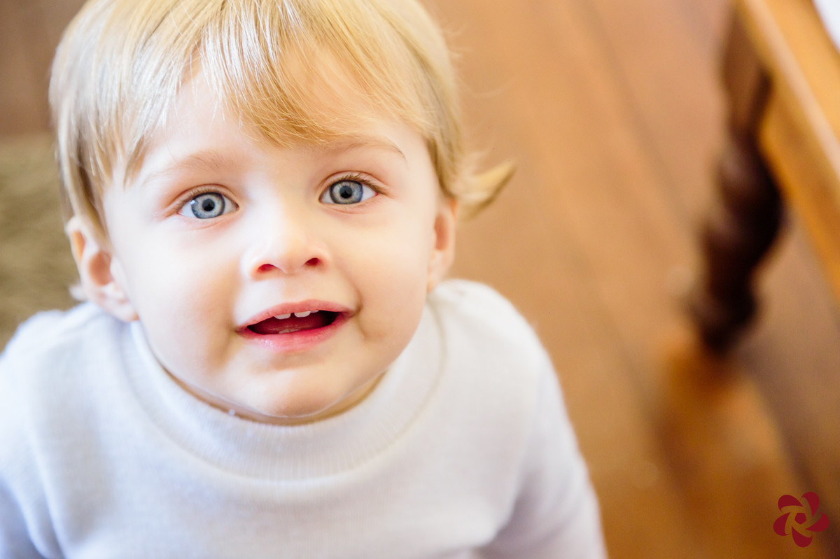 Otávio está olhando para a câmera com seus olhos azuis brilhantes sorrindo, deixando aparecer dois pequenos dentes.