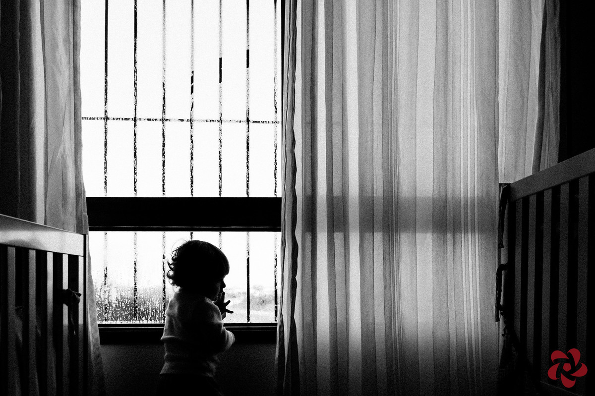 Em seu quarto, Otávio olha pela janela depois de brincar no vidro suado.