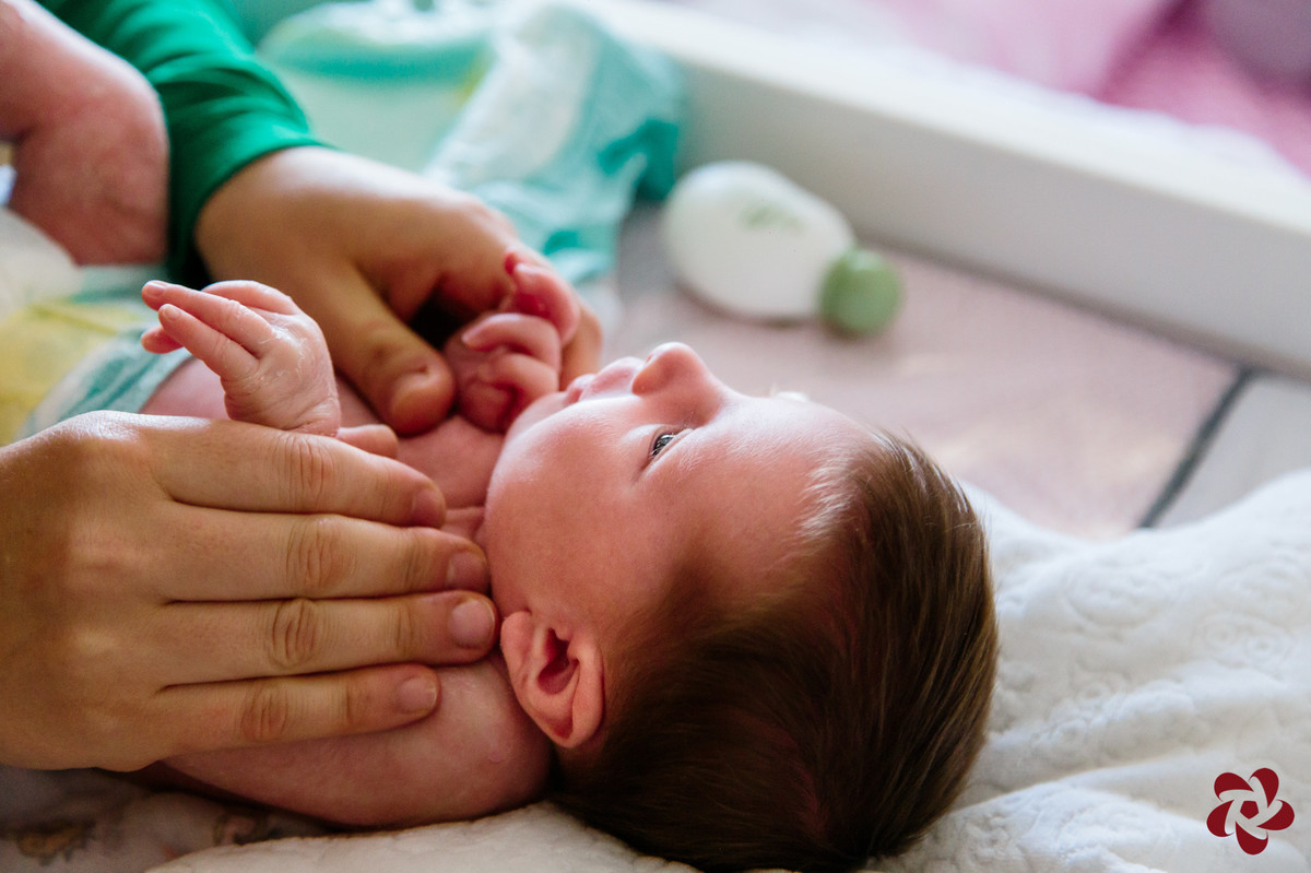 Júlia está deitada em um trocador, olhando com atenção para sua mãe, enquanto a mamãe tira sua roupa.