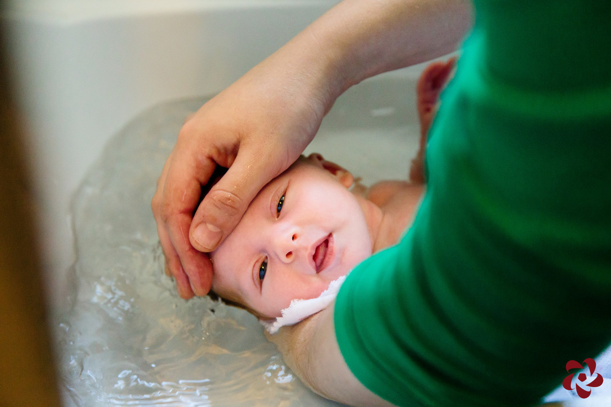 Natácia está dando banho em Júlia em uma banheira e a bebê está olhando para a câmera, passando a sensação de que está gostando.