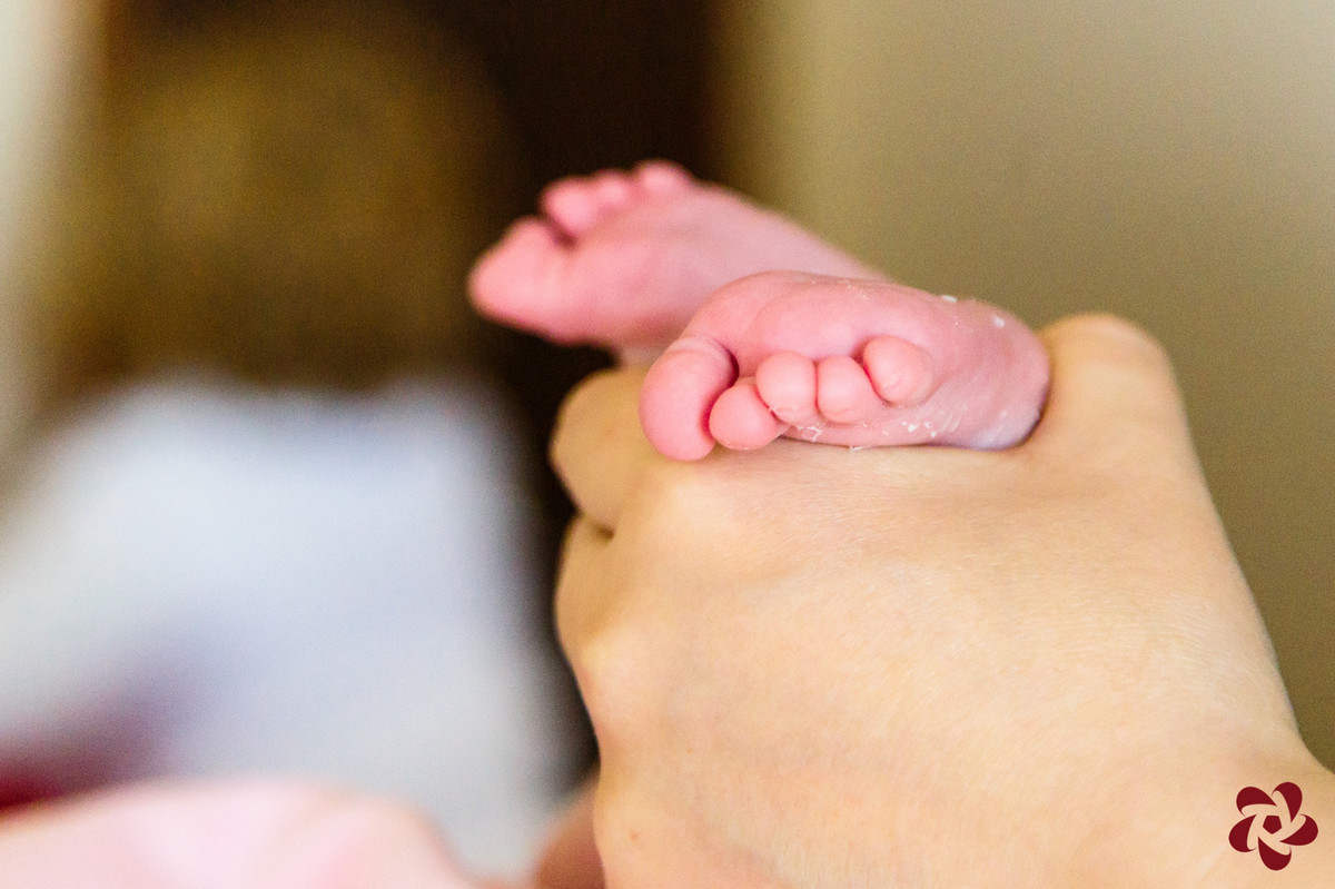 Close dos pés da bebê que estão sendo segurados pela mãe.