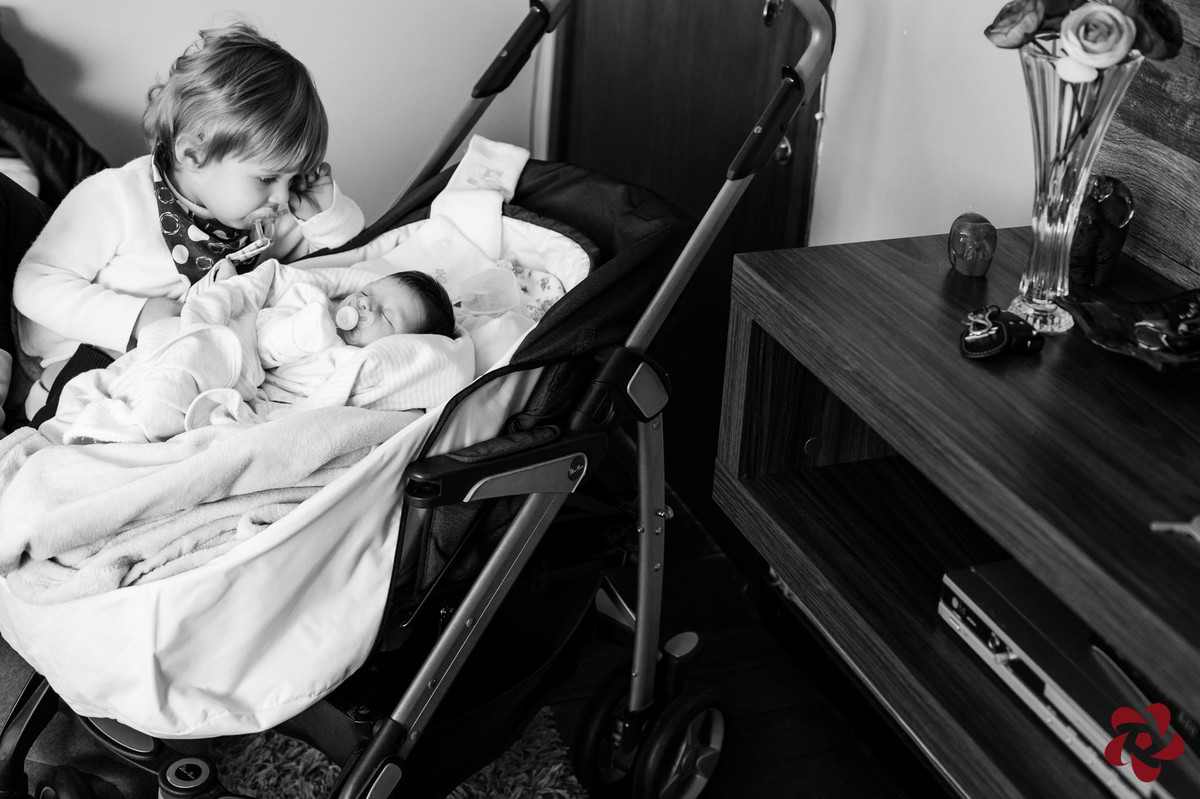 O irmão mais velho observa a irmã recém chegada que está deitada no carrinho.