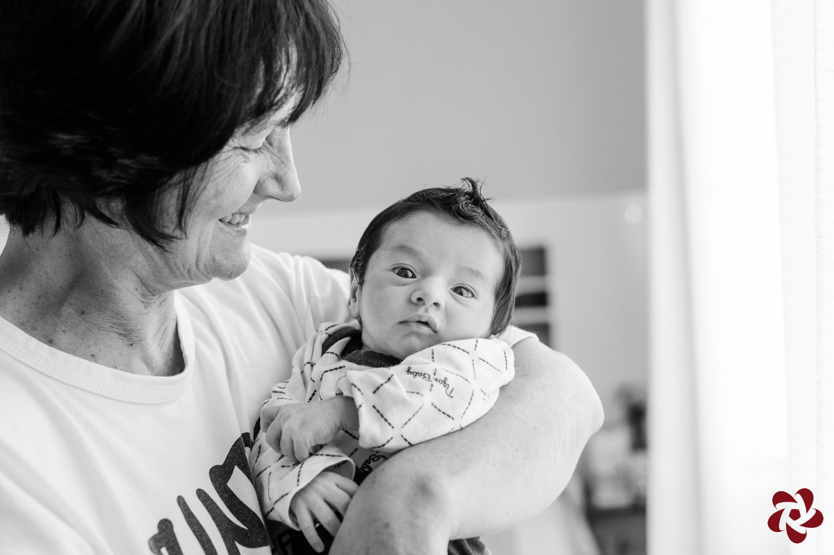 Foto em preto e branco. Após o banho Henrique está vestido e penteado no colo da avó. A avó olha para o bebê enquanto o bebê olha para a câmera fotográfica.