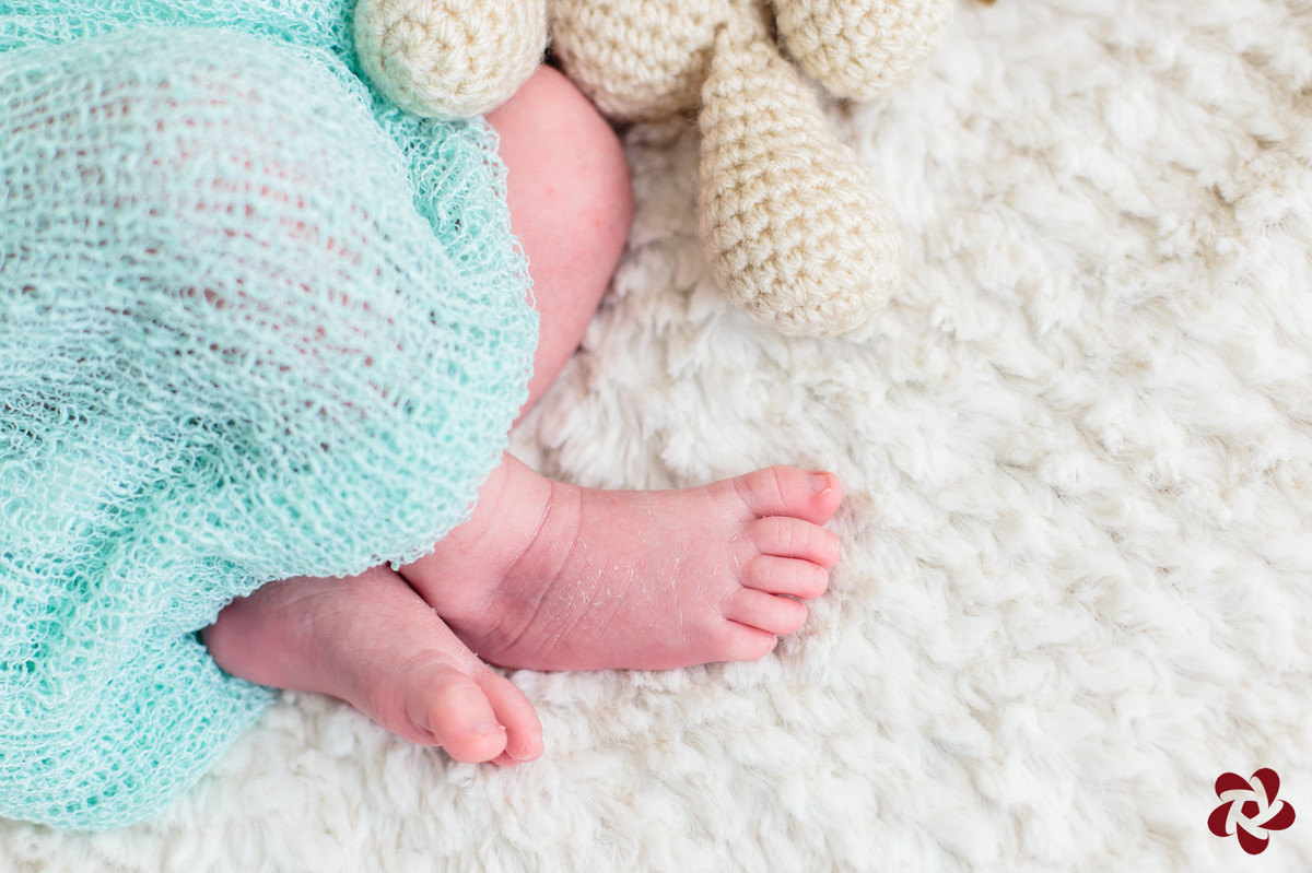 Detalhe dos pés do Henrique dobrados de lado um em cima do outro, sobre um cobertor bege claro, tapado com um wrap verde água