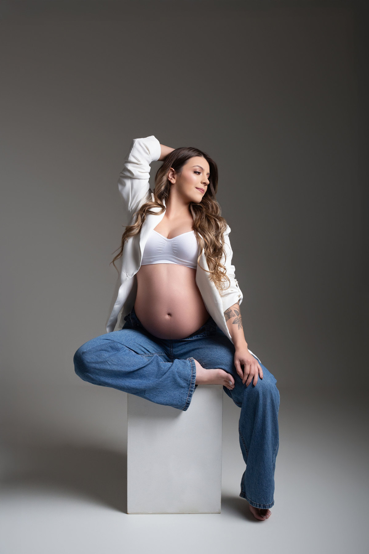 ensaio fotográfico gestante, pose de gestante sentada, pose de gestante no cubo, foto de gestante calça jeans 
