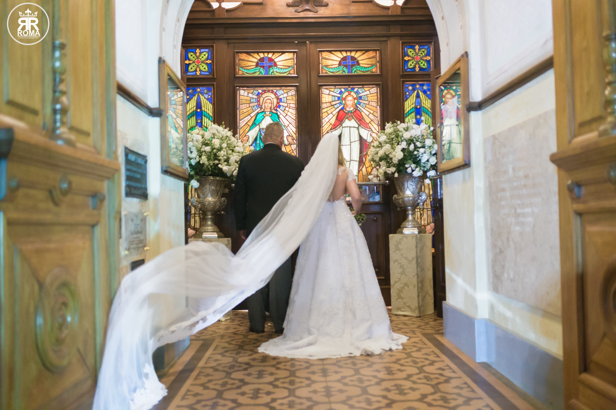 noiva de braços dados ao seu pai na porta da igreja esperando a abertura das portas do templo