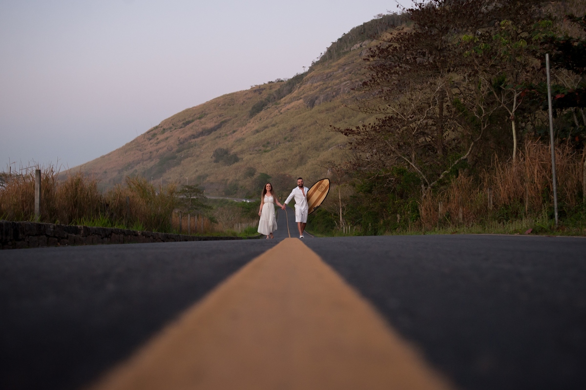 Noivos caminhando na estrada de mãos dadas junto com uma prancha 