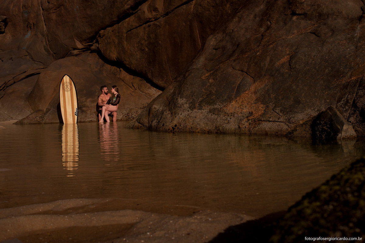 Noivos namorando na praia do Secreto com uma prancha de surfe do lado.