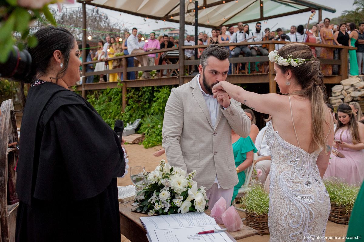 foto do noivo beijando a mão da noiva em cerimônia com juíza de paz