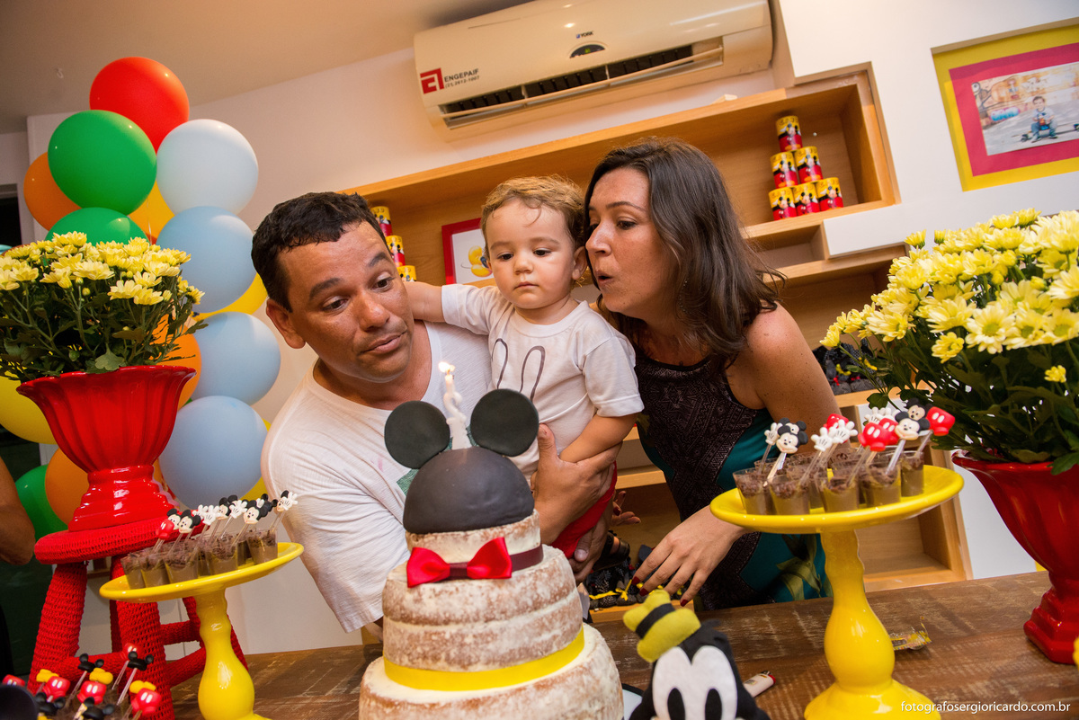 criança assoprando a vela de aniversário junto com os pais