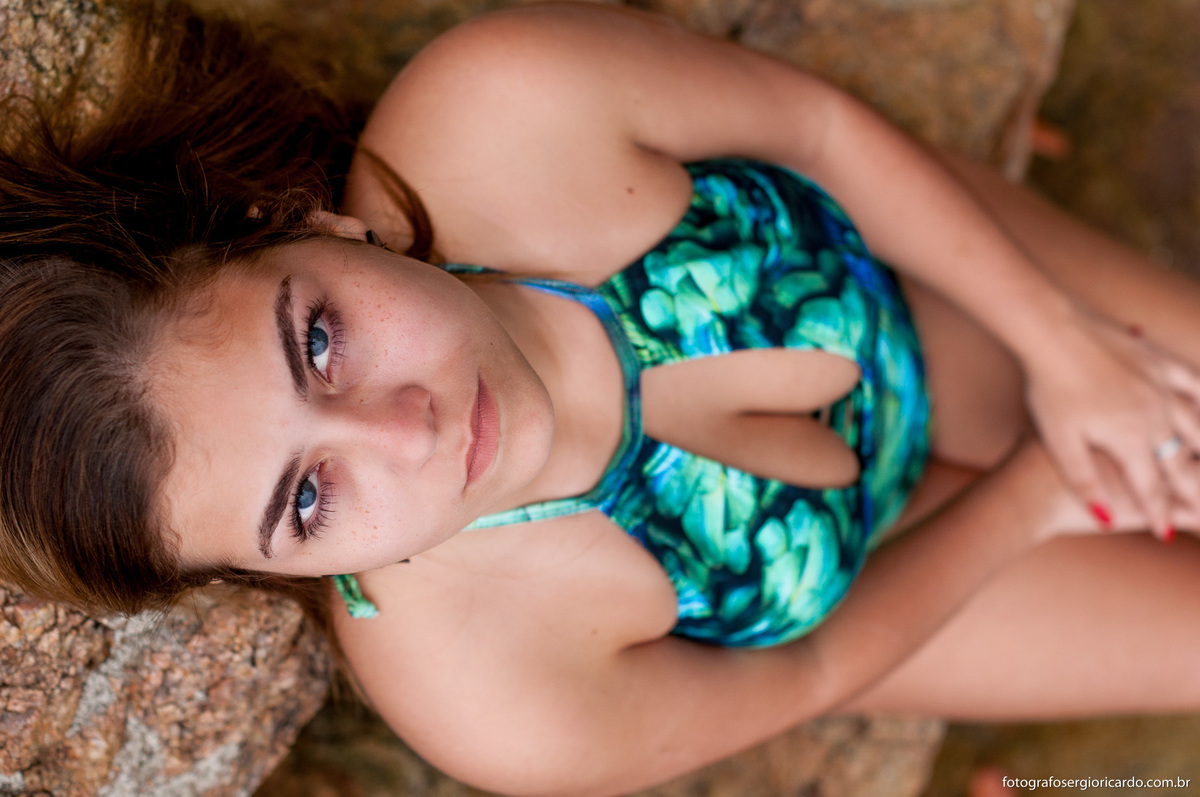 foto da debutante na praia da joatinga encostada na pedra olhando para a lente