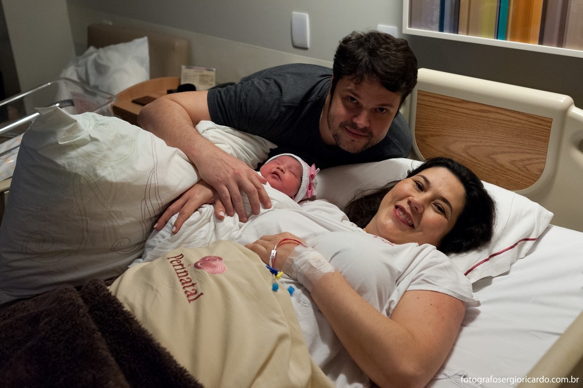 Fotografia dos pais com criança recém-nascida no quarto da Perinatal Barra no Rio de Janeiro