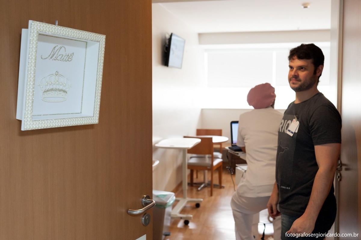 Pai colocando enfeite da porta do quarto para a chegada da filha na Perinatal Barra no Rio de Janeiro