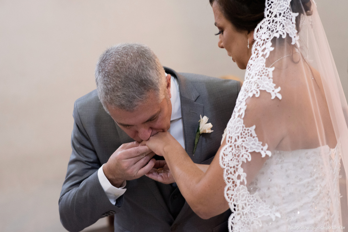 fotografia do noivo beijando a mão da noiva com a aliança durante o casamento na igreja nossa senhora do loreto