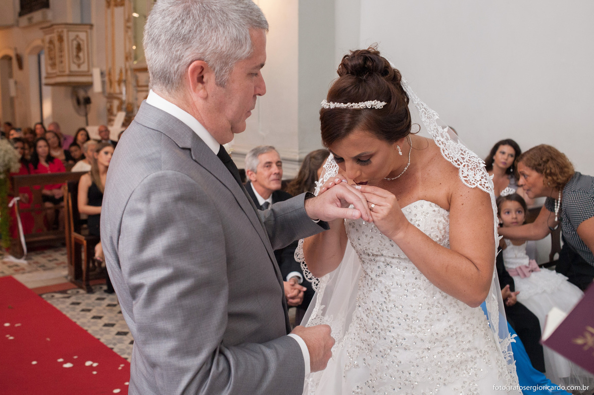 fotografia da noiva beijando a mão do noivo com a aliança durante o casamento na igreja nossa senhora do loreto
