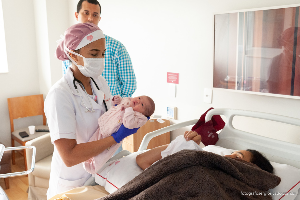 Fotografia de enfermeira levando a criança recém-nascida para a primeira mamada no quarto da Perinatal Barra no Rio de Janeiro