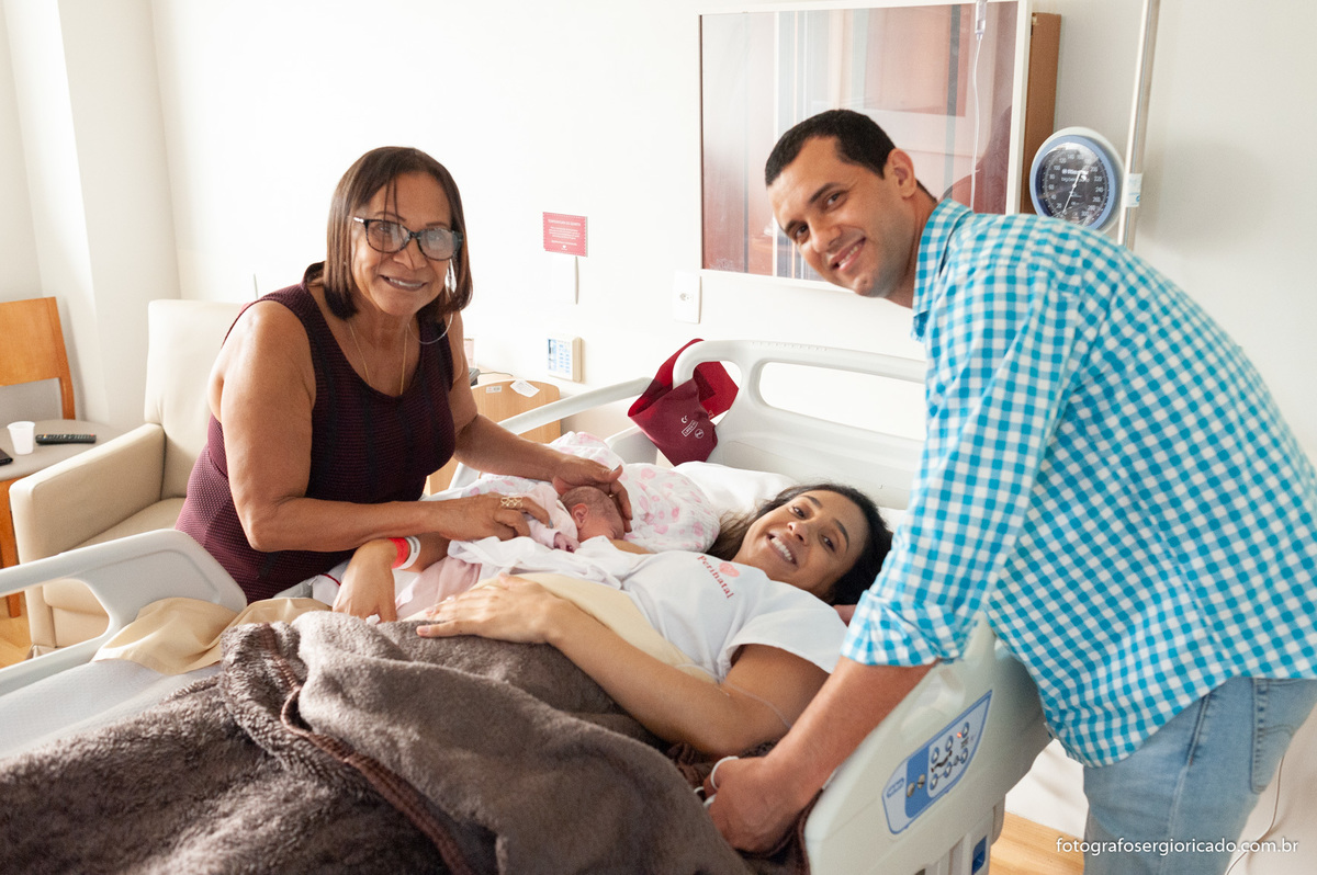 Fotografia dos pais e avó com criança recém-nascida no quarto da Perinatal Barra no Rio de Janeiro