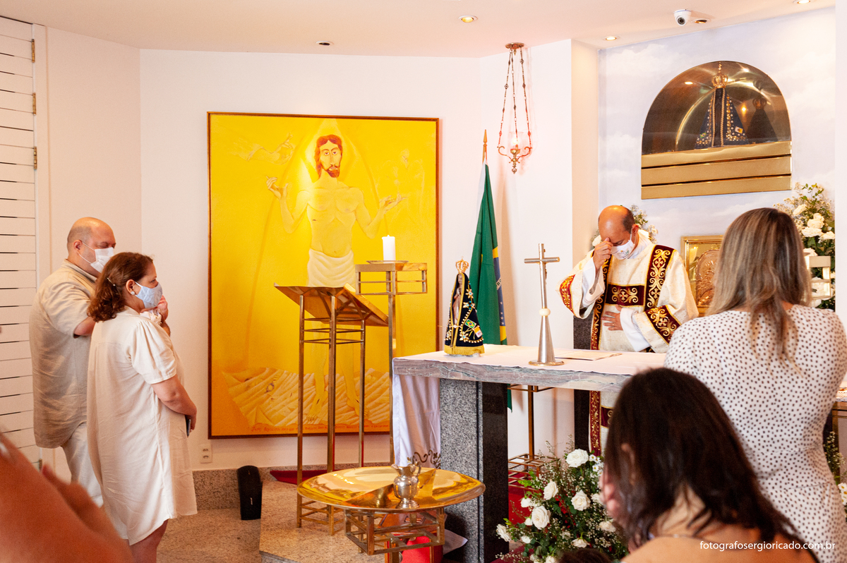 Foto dos pais com o padre realizando cerimônia de batismo na Capela de Nossa Senhora Aparecida no Cristo Redentor localizado no Morro do Corcovado no Rio de Janeiro