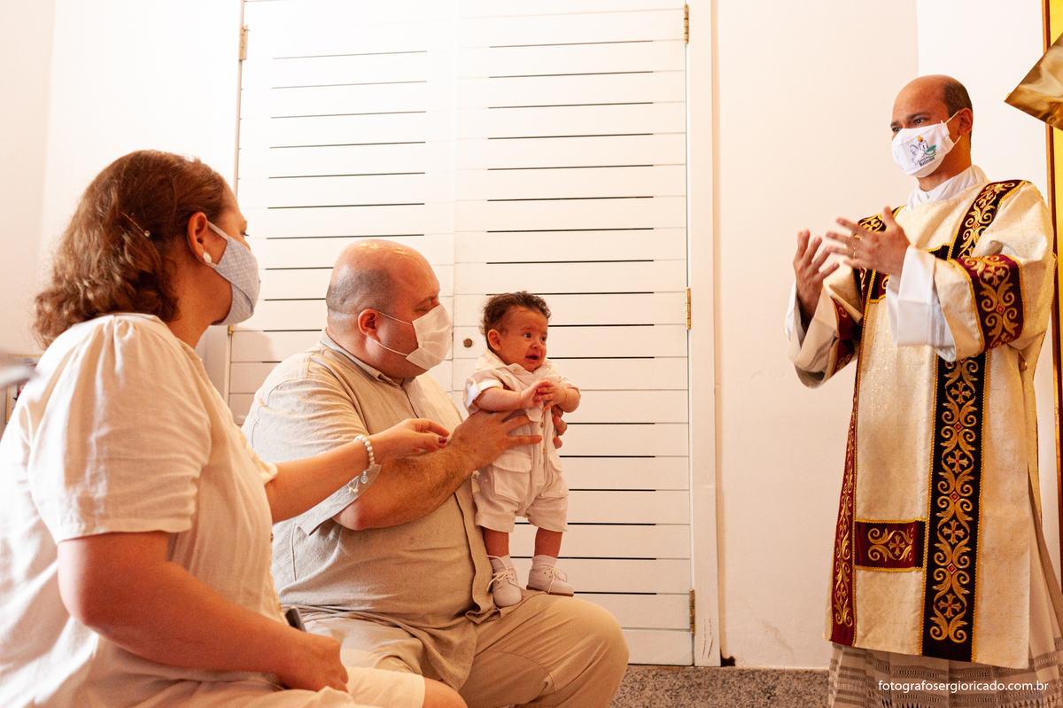 Fotografia dos pais com criança recebendo o batismo na Capela de Nossa Senhora Aparecida no Cristo Redentor localizado no Morro do Corcovado no Rio de Janeiro