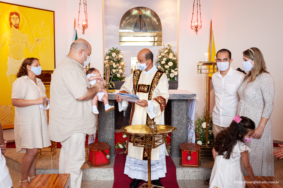 Fotografia dos pais com o padre realizando cerimônia de batismo na Capela de Nossa Senhora Aparecida no Cristo Redentor localizado no Morro do Corcovado no Rio de Janeiro