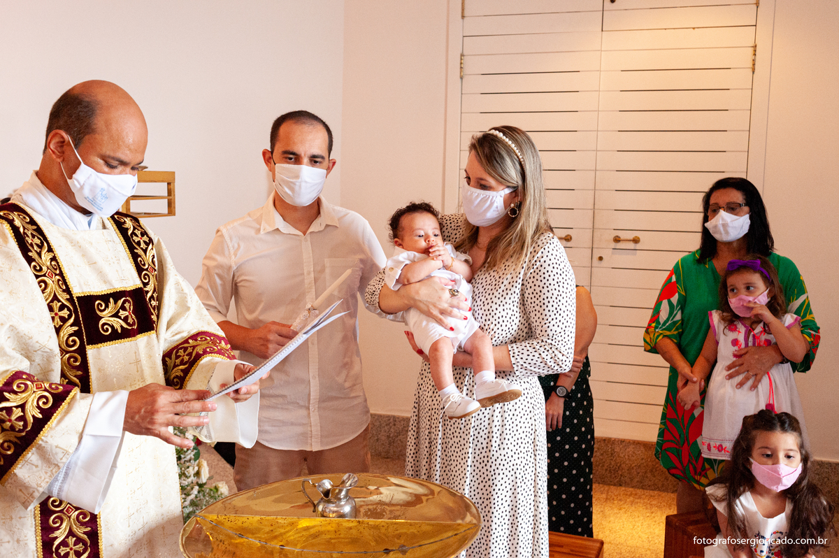 Fotografia do padre com padrinhos e convidados realizando cerimônia de batismo na Capela de Nossa Senhora Aparecida no Cristo Redentor localizado no Morro do Corcovado no Rio de Janeiro