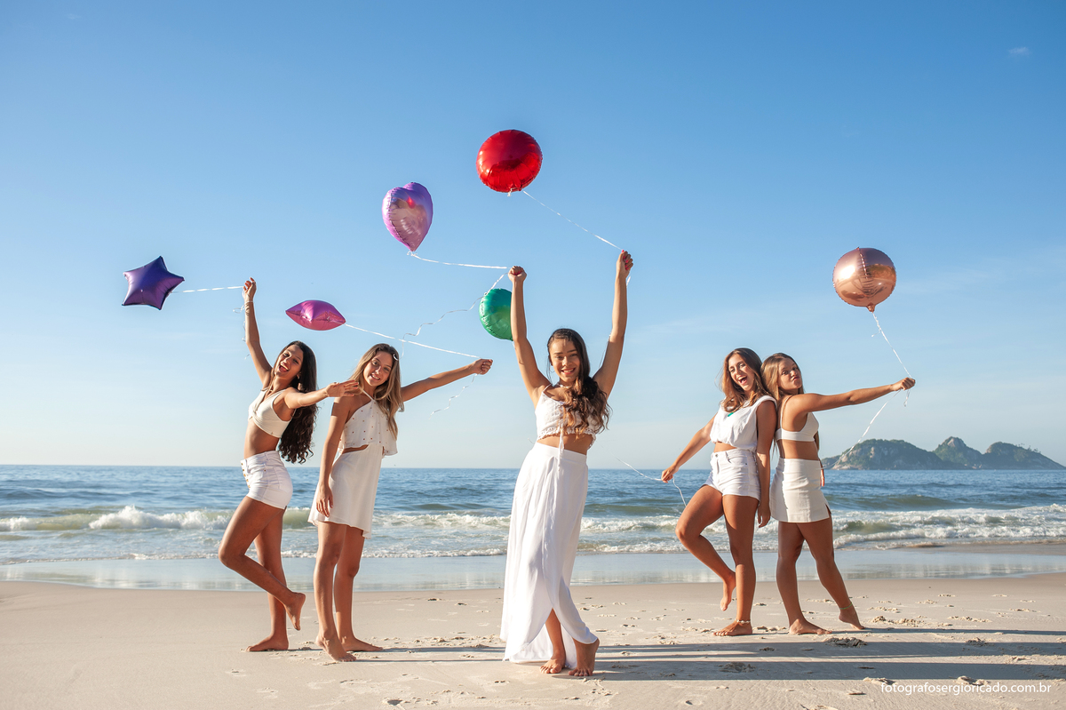 fotografia de ensaio de 15 anos com amigas segurando balões de gás coloridos na praia da joatinga no rio de janeiro