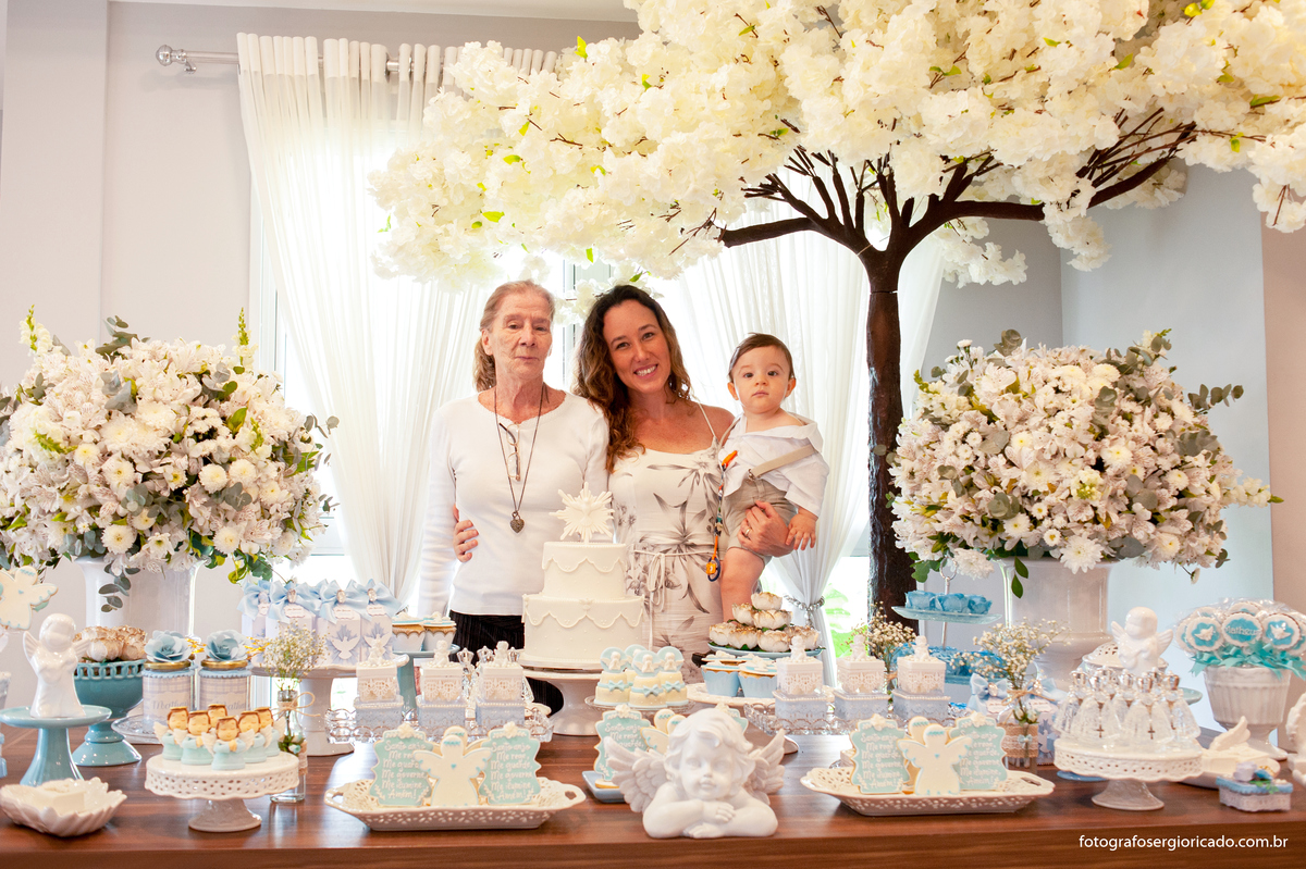 Fotografia da mãe e avó com o filho no colo na mesa decorada em festa de batismo na Barra da Tijuca no Rio de Janeiro 
