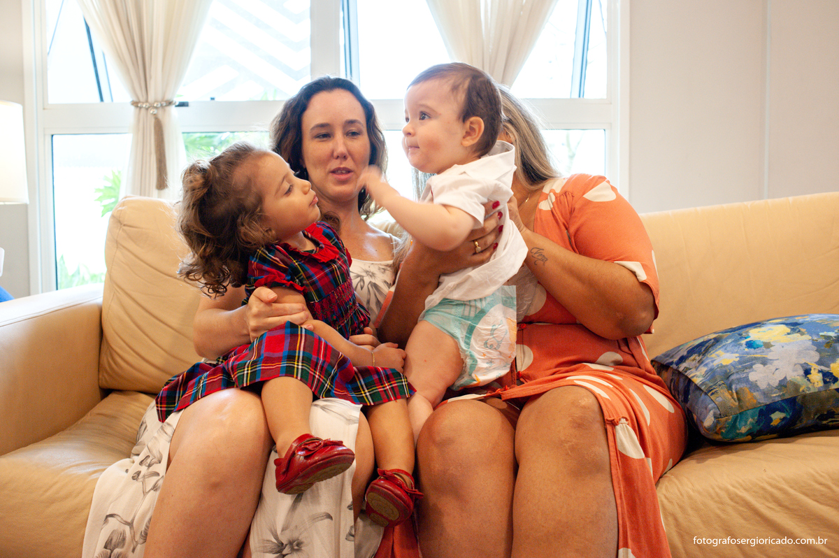 Fotografia das mães com os filhos no colo brincando durante a festa de batismo na Barra da Tijuca no Rio de Janeiro 