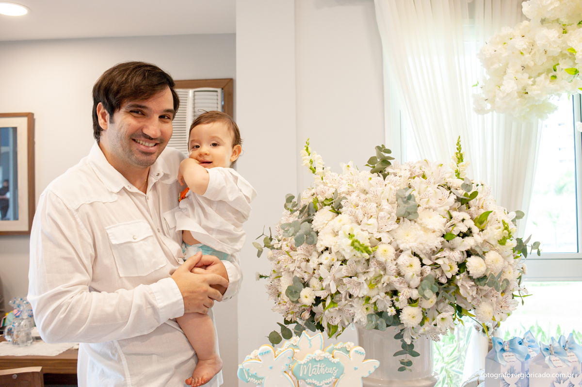Fotografia do pai com filho no colo durante festa de batismo na Barra da Tijuca no Rio de Janeiro 