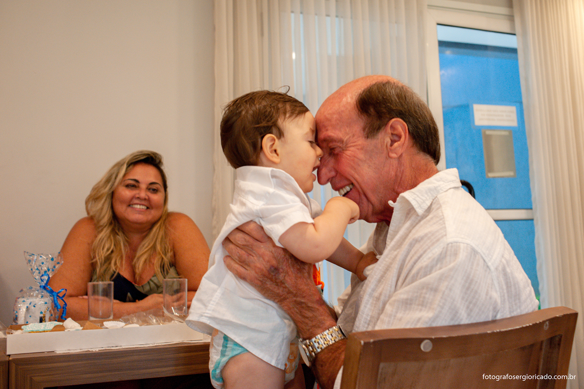 Fotografia do avô com neto no colo durante festa de batismo na Barra da Tijuca no Rio de Janeiro 